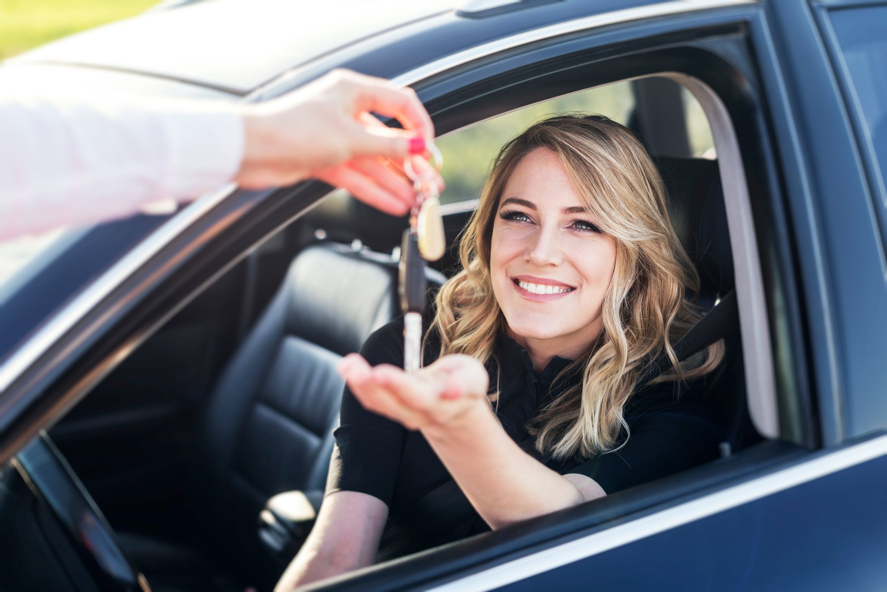 An attractive woman in a car gets the car keys. Rent or purchase of auto